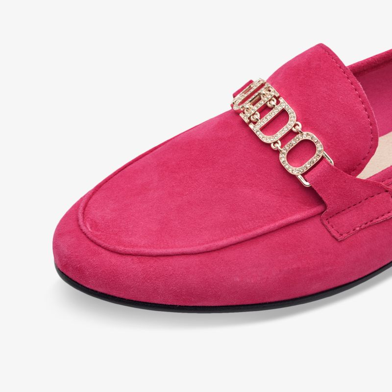 Detailaufnahme eines pinken Veloursleder-Slippers mit funkelndem Schmuck-Logo und feiner Naht