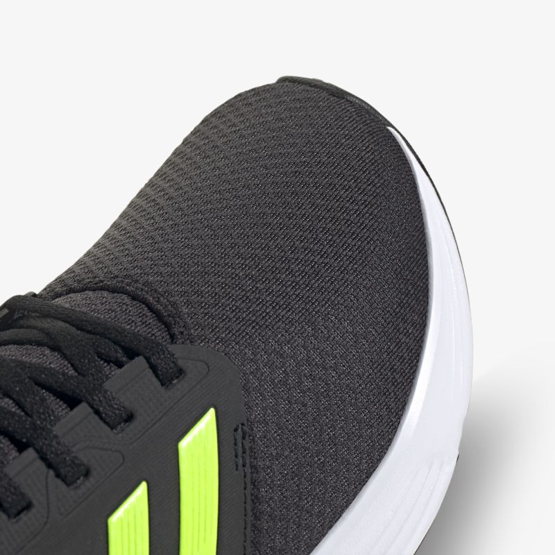 Schwarzer Sportschuh mit neon Details, eng geflochtenem Obermaterial und robuster weißer Sohle im Detailblick.