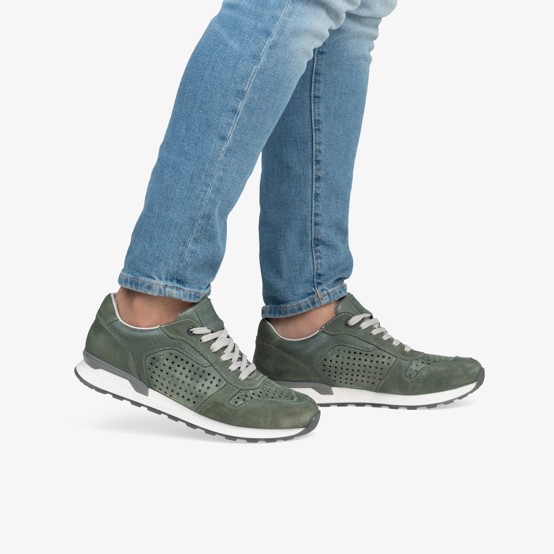 Grüne sportliche Freizeitschuhe mit perforiertem Obermaterial und flexibler Laufsohle, getragen an Füßen mit Jeans