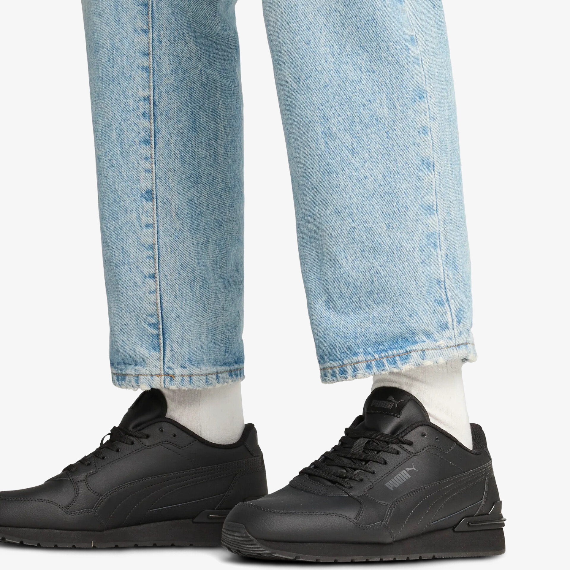 Schwarze sportliche Schuhe aus Leder mit Schnürsenkeln, getragen an den Füßen mit weißen Socken und Jeans