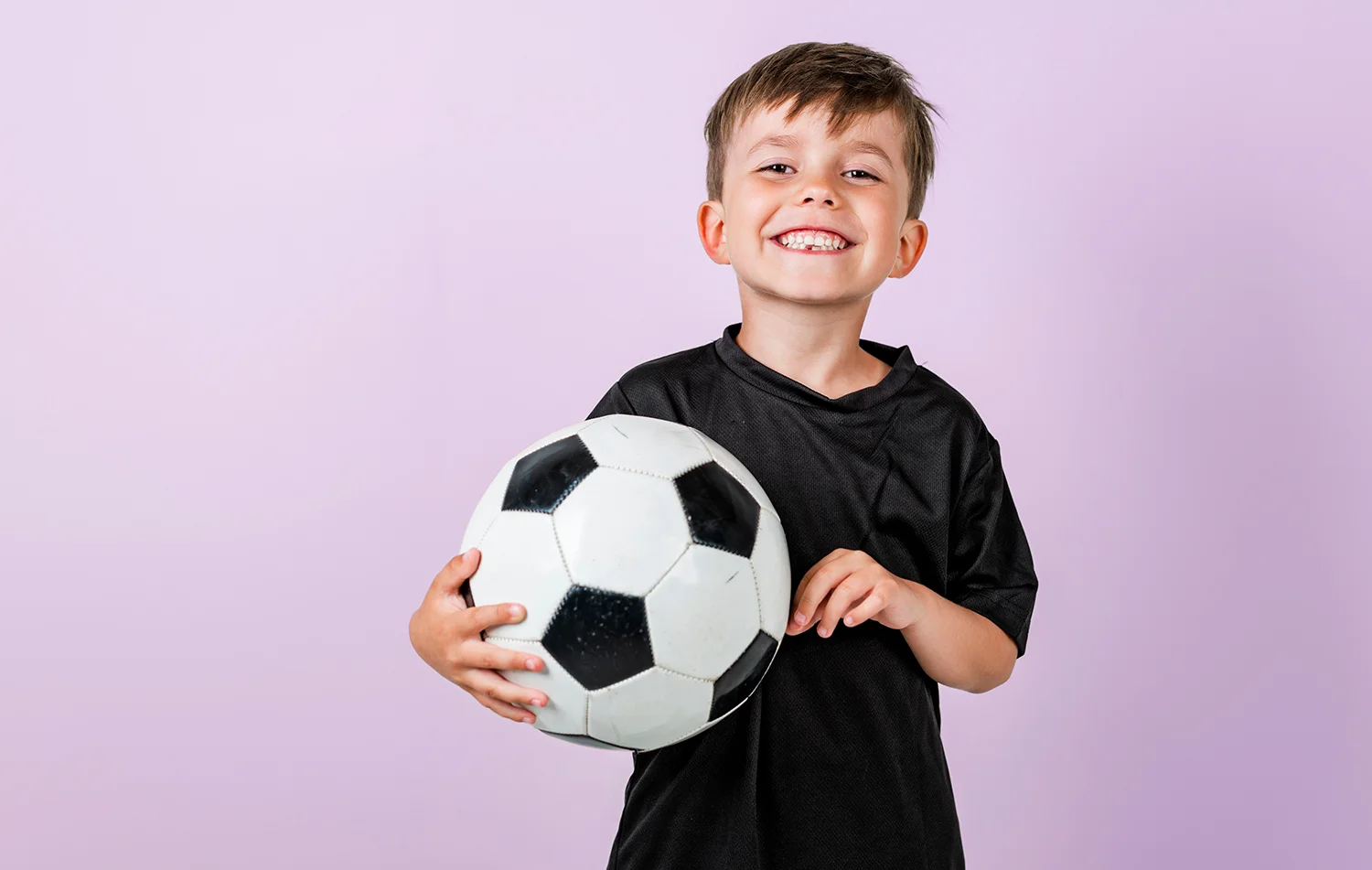 Lächelnder Junge in schwarzem Trikot hält einen schwarz-weißen Fußball vor hellem Hintergrund