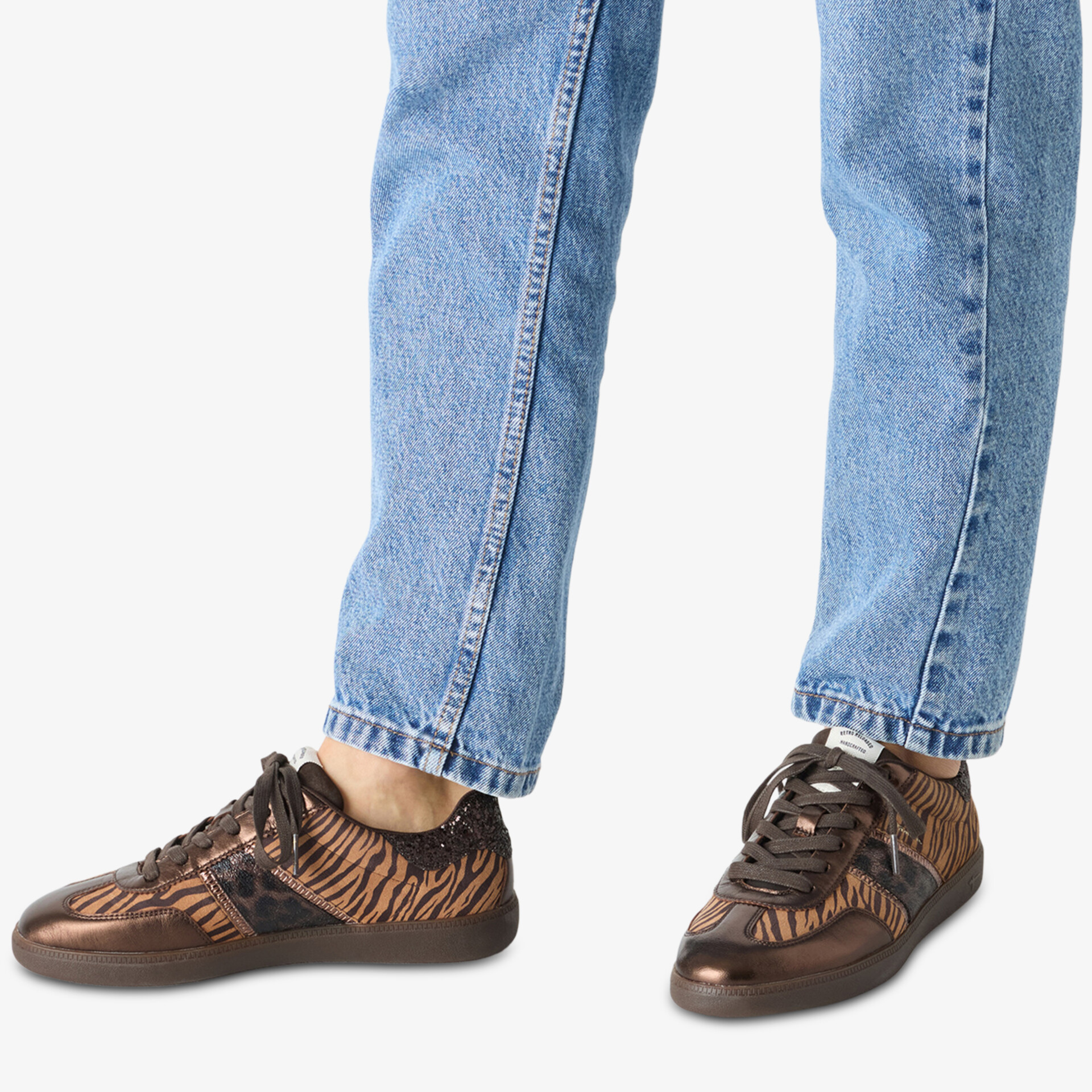 Modische braune Sneaker mit dezent gemustertem Obermaterial, bequem und flexibel, getragen an Füßen mit Jeans