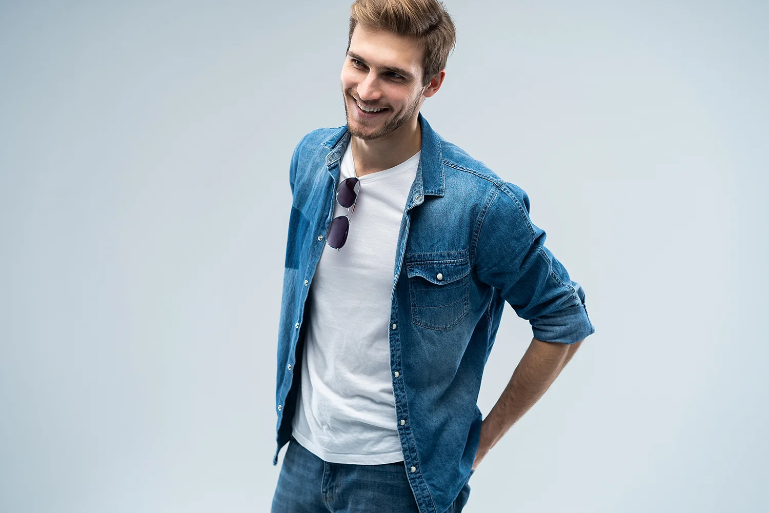 Lächelnder Mann trägt offenes blaues Jeanshemd über weißem T-Shirt mit Sonnenbrille am Kragen