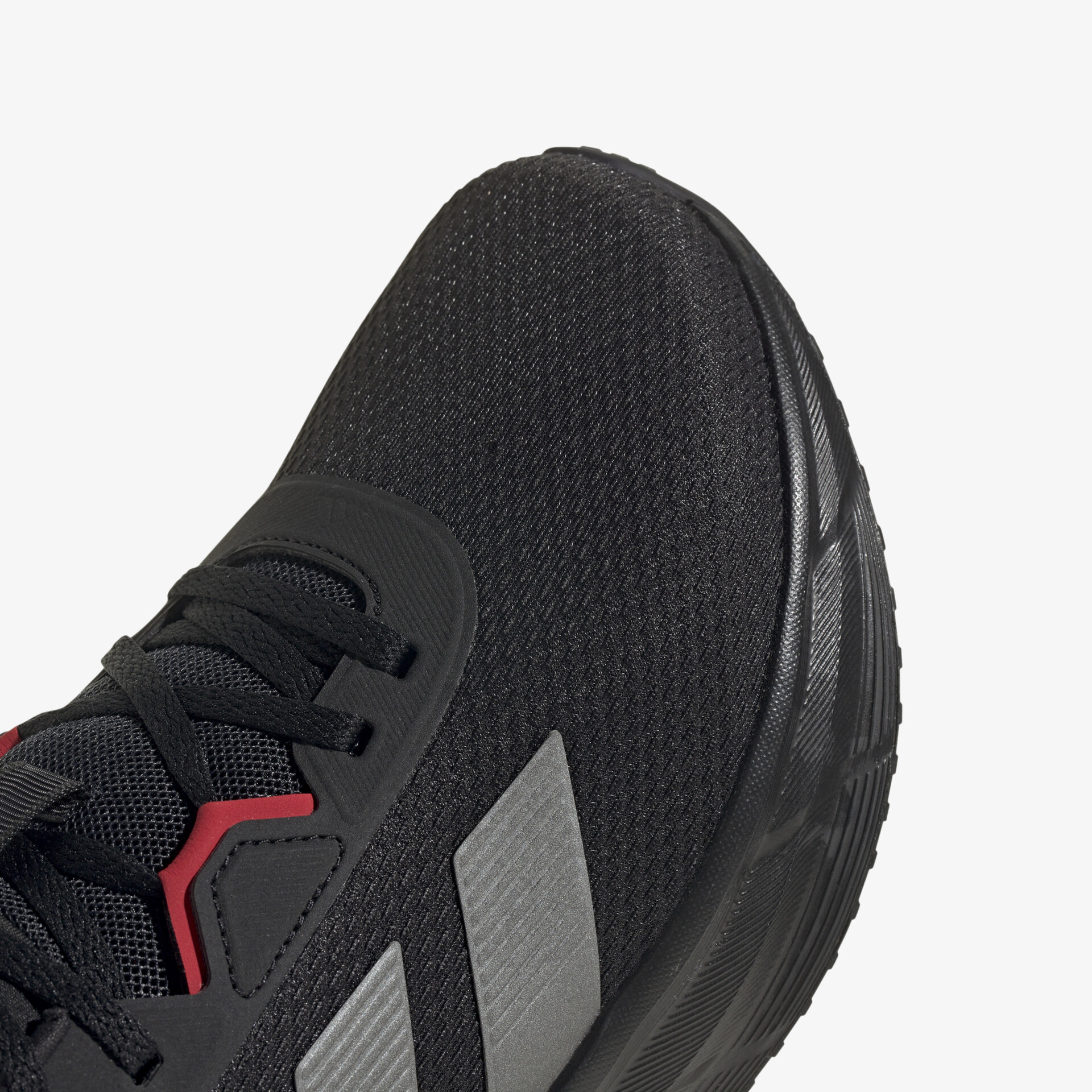 Detailaufnahme eines schwarzen Sportschuhs mit roten Akzenten, leichte Textur und flexible Schnürung sichtbar