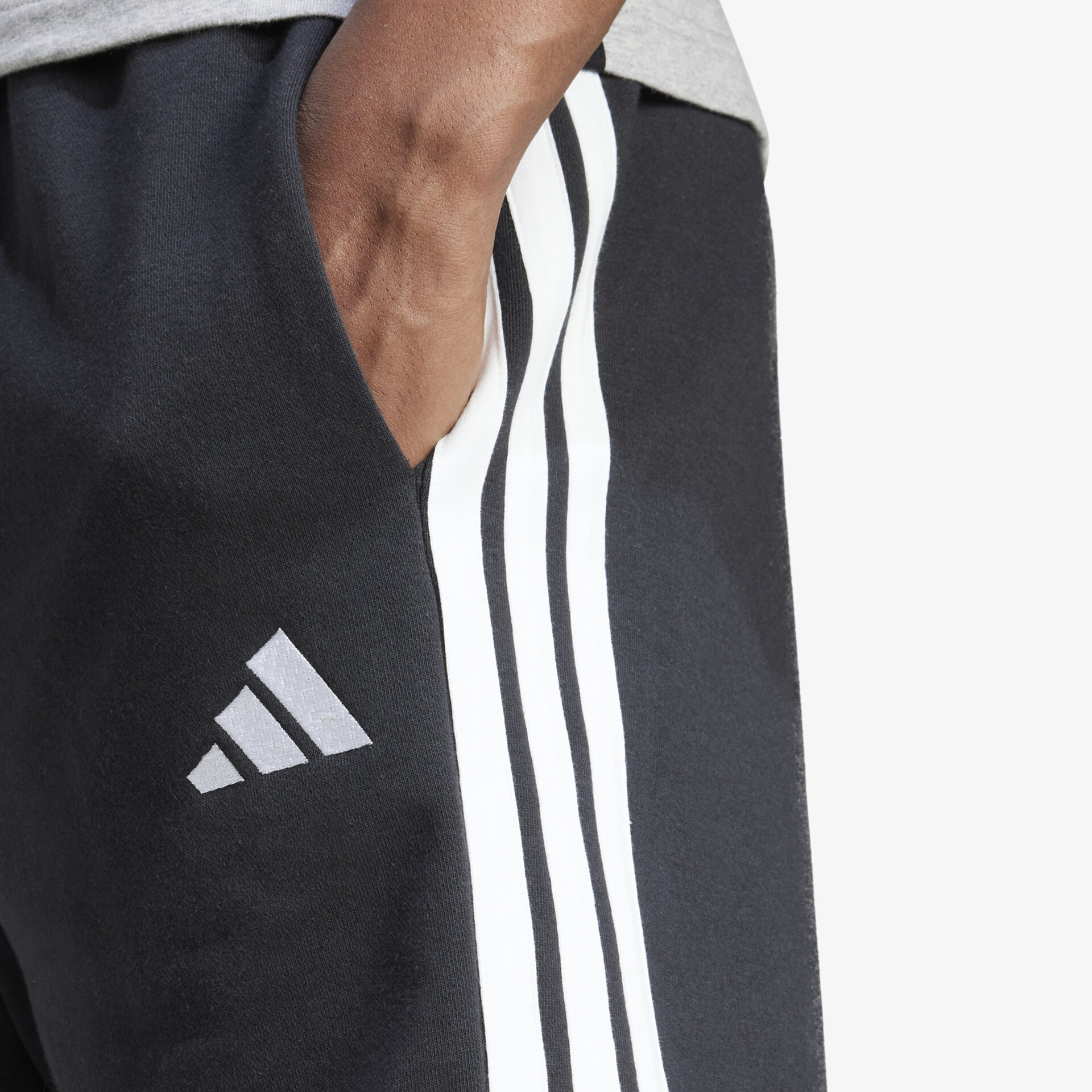 Detailaufnahme der sportlichen schwarzen Hose mit markanten weißen seitlichen Streifen und Adidas Logo