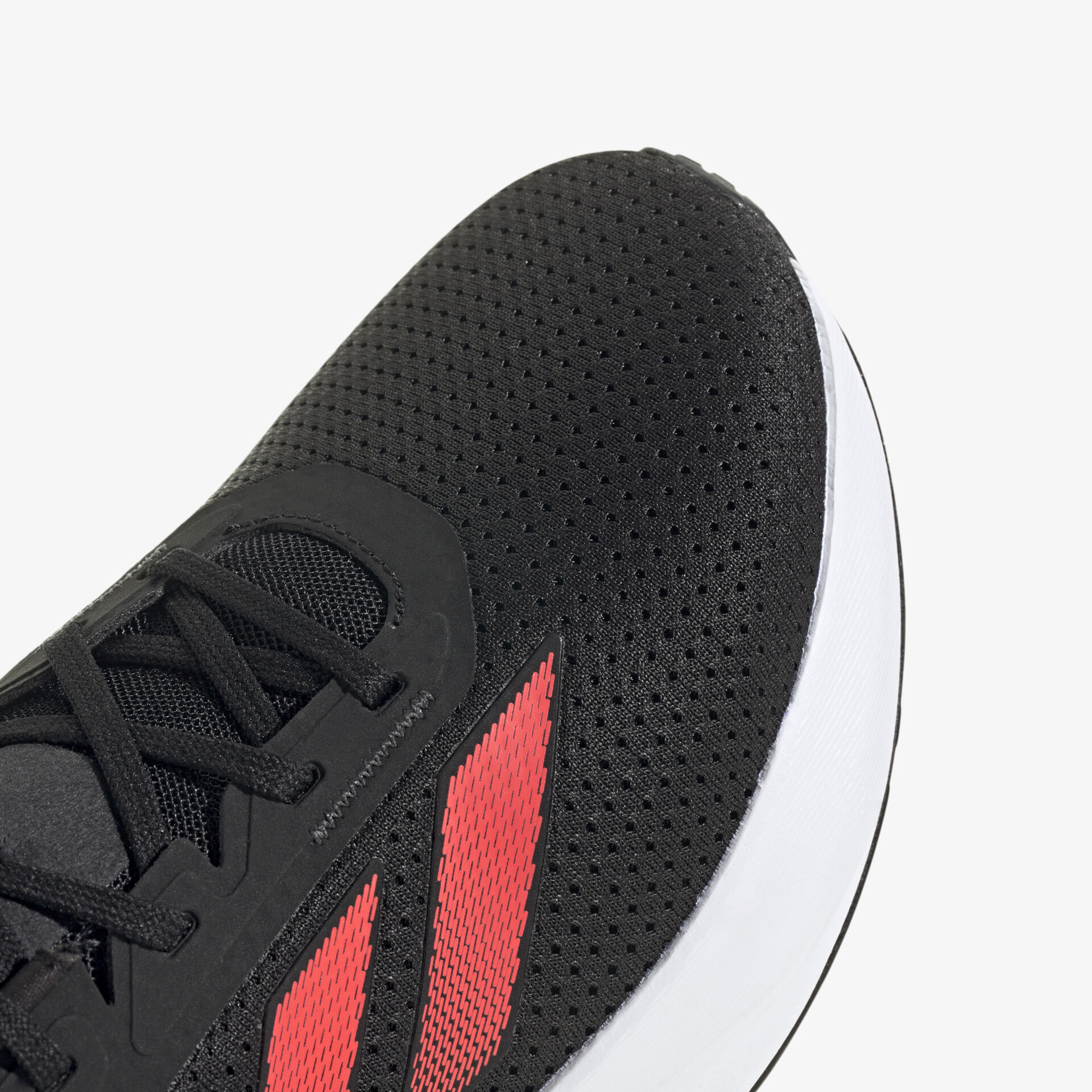 Detailaufnahme eines schwarzen Sportschuhs mit rotem Streifendetail und weißer rutschfester Laufsohle