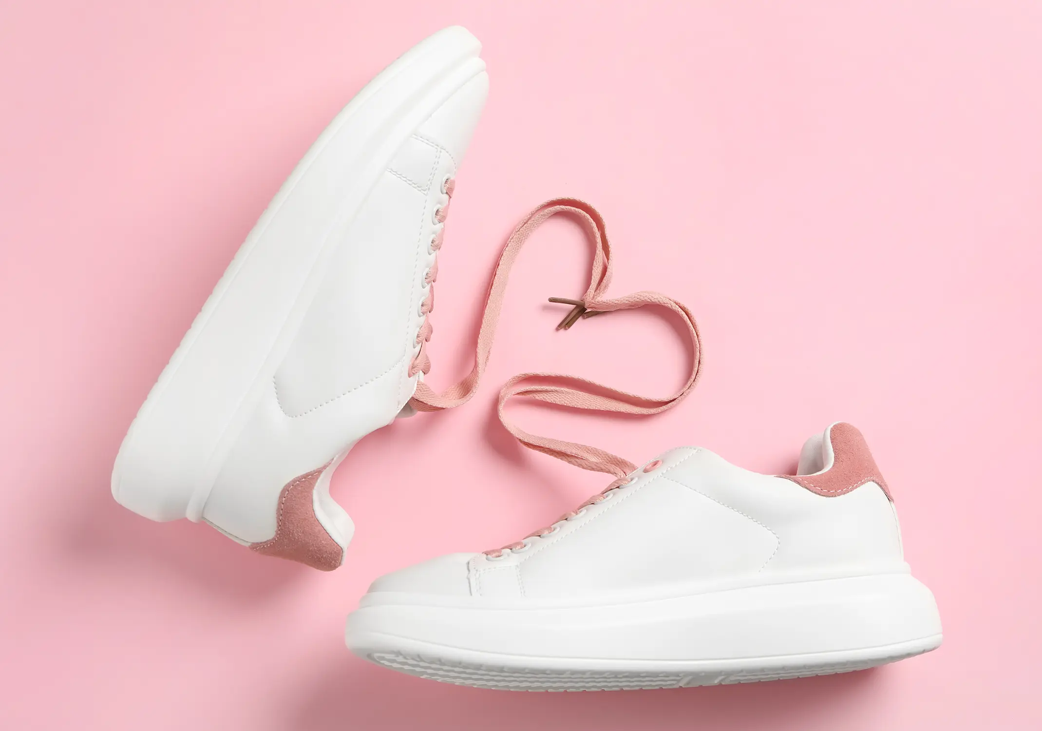 Weiße Sneaker mit rosa Details und Schnürsenkeln, die zu einem Herz geformt sind, auf rosa Hintergrund