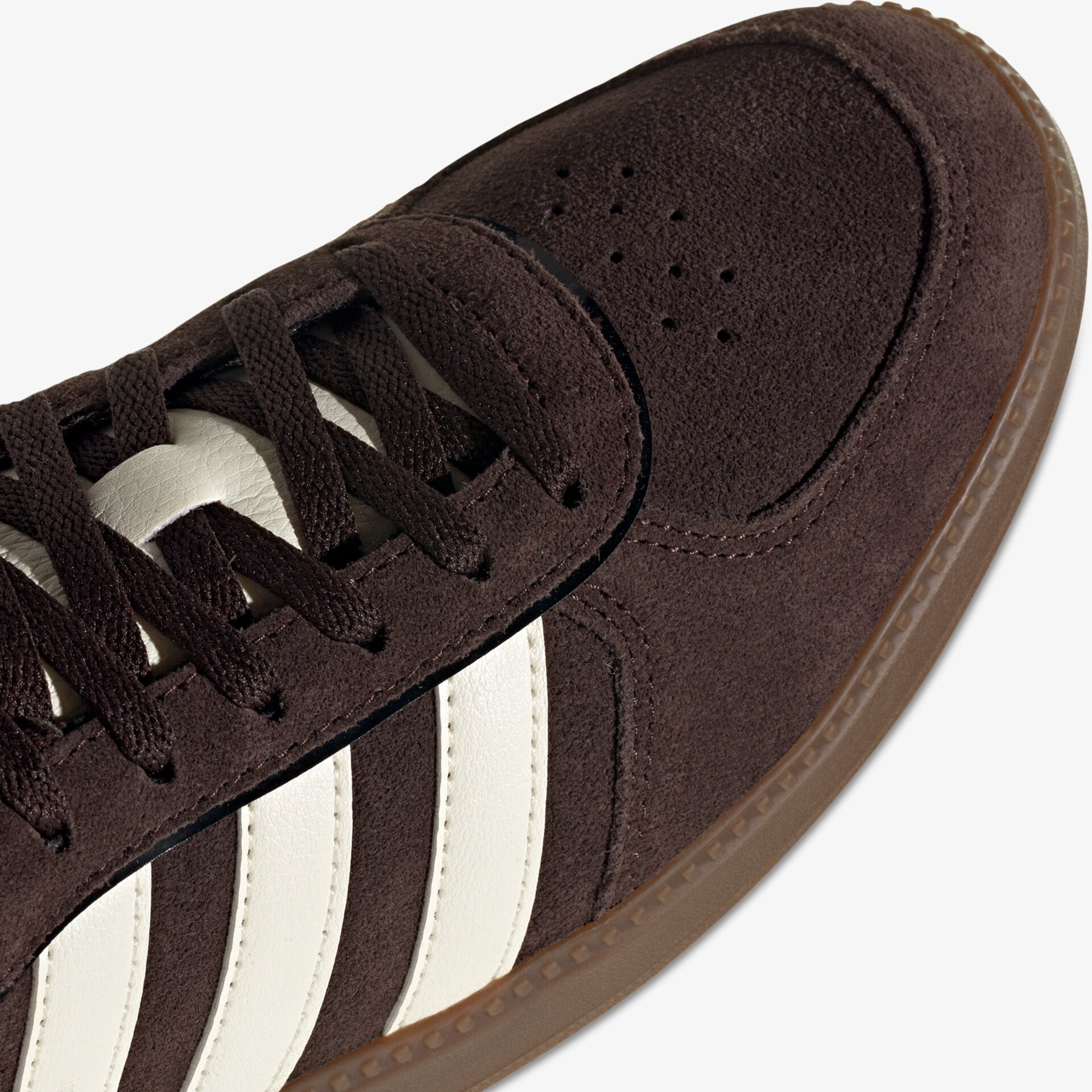 Detailaufnahme des vorderen Bereichs eines braunen Wildleder-Sneakers mit weißen Streifen und Schnürsenkeln