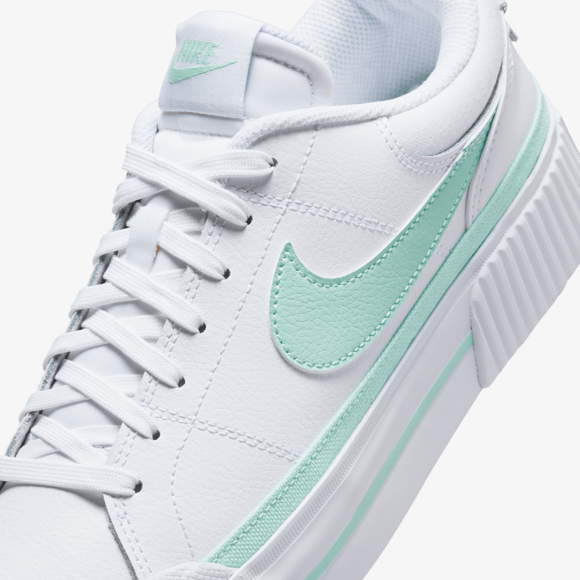 Detailaufnahme eines weißen Sneakers mit grünem Nike-Logo und präziser Schnürung, hochwertiges Material sichtbar