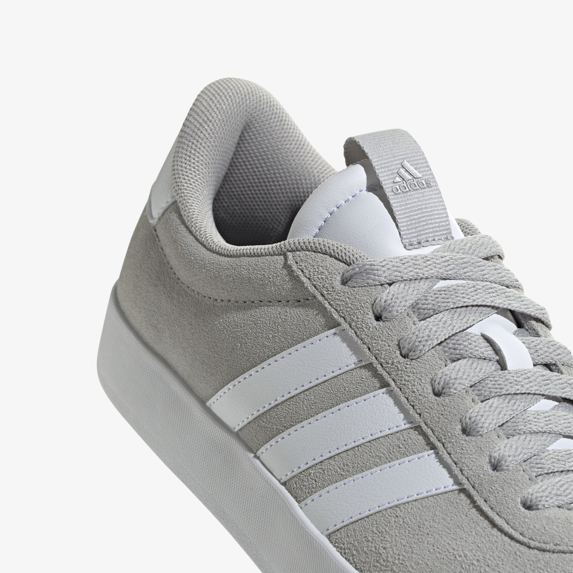 Detailaufnahme eines grauen Sneakers mit weißen Streifen und Schnürsenkeln, weiches komfortables Material