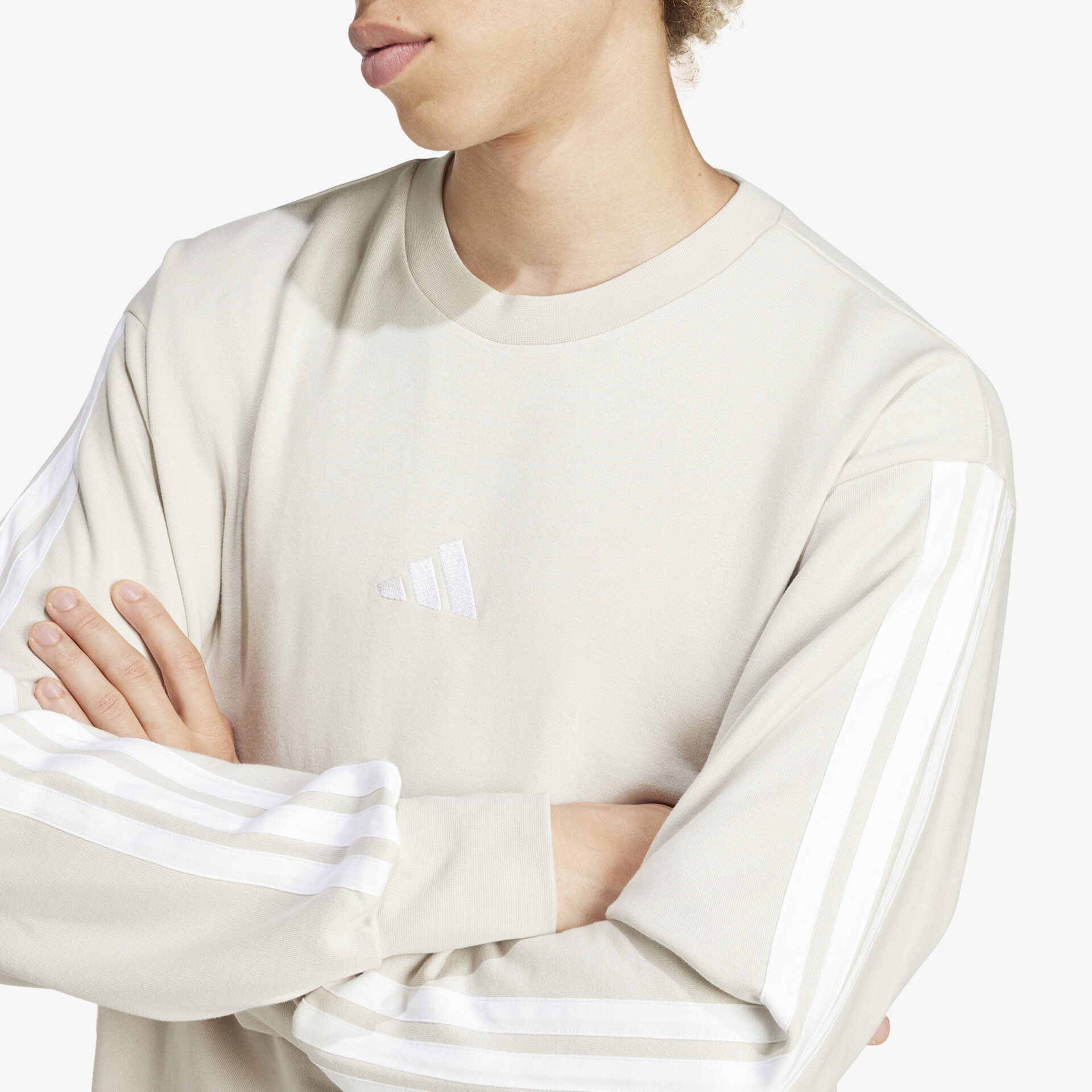 Beiger Pullover mit drei weißen Streifen an den Ärmeln, sportlicher Schnitt und weiches Material getragen