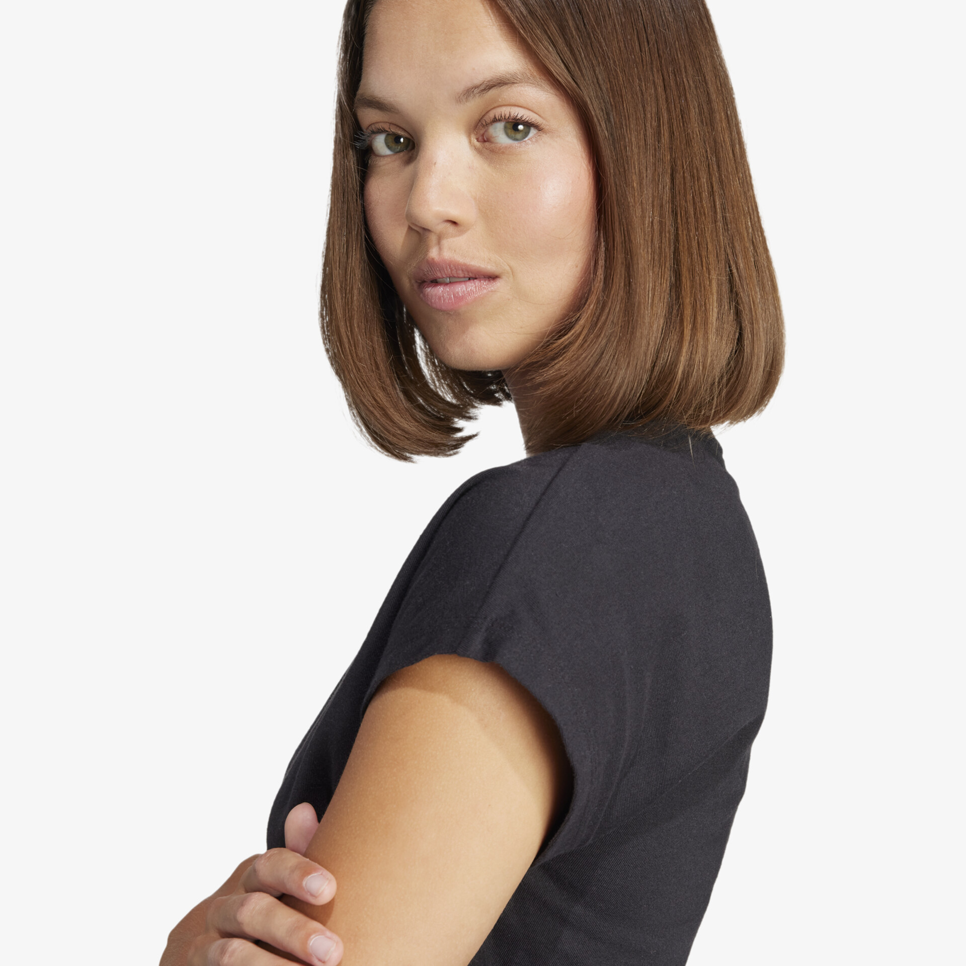 Porträt einer Person mit schulterlangem Haar und schlichtem schwarzem Shirt vor neutralem Hintergrund.