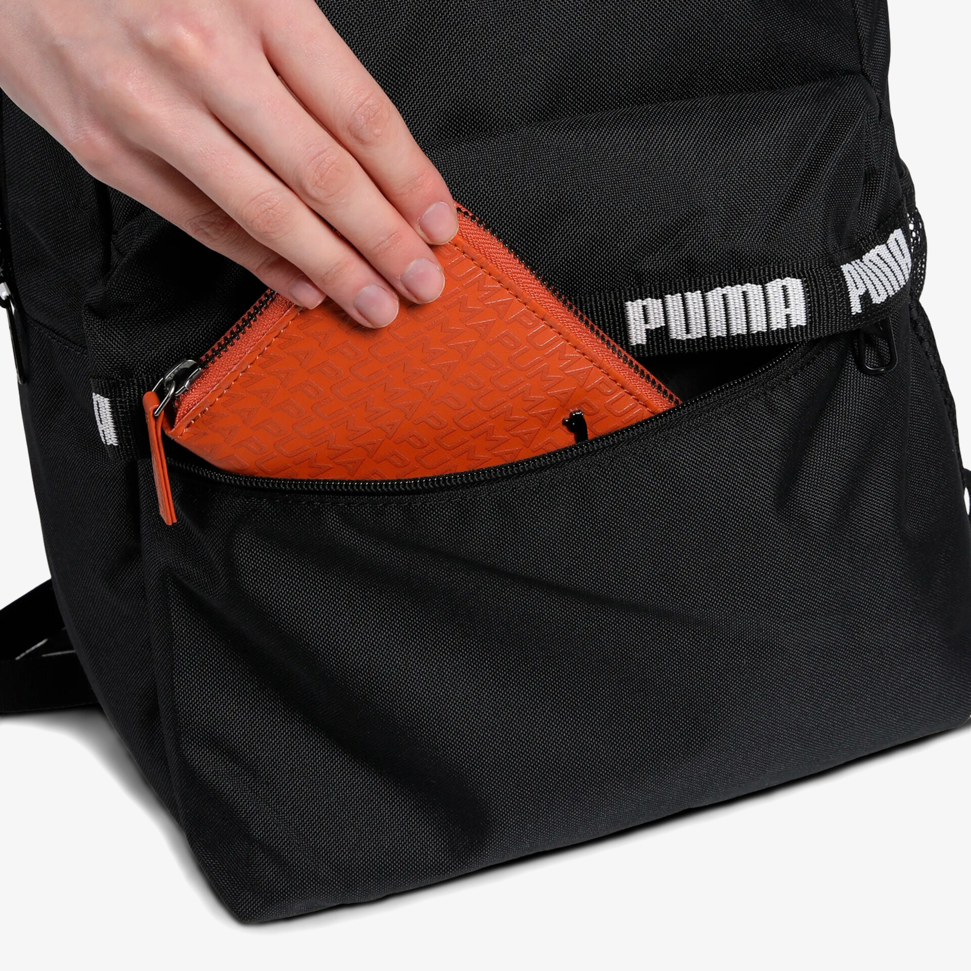 Hand legt orangenes Portemonnaie in schwarze Reißverschlusstasche eines Rucksacks, praktisch und modern