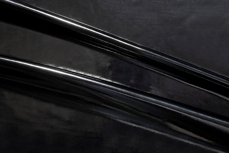 Glänzendes schwarzes Lackleder mit glatten, reflektierenden Oberflächen und feinen Falten
