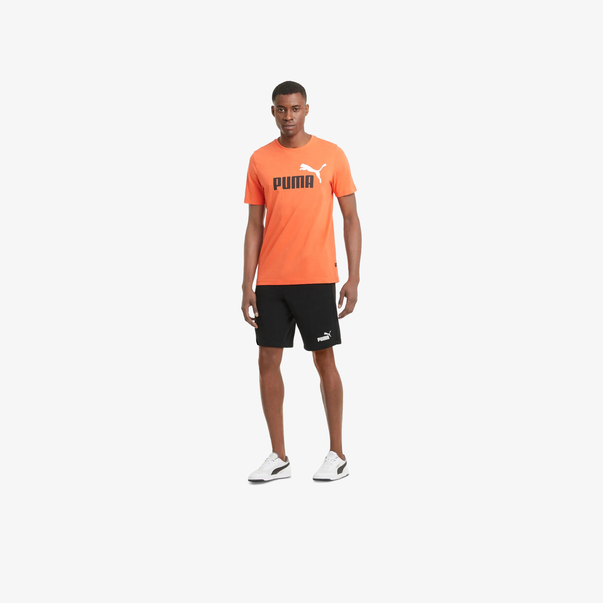 Sportliches Outfit mit orangefarbenem Shirt, schwarzen Shorts und weißen Sportschuhen, bequem und funktional