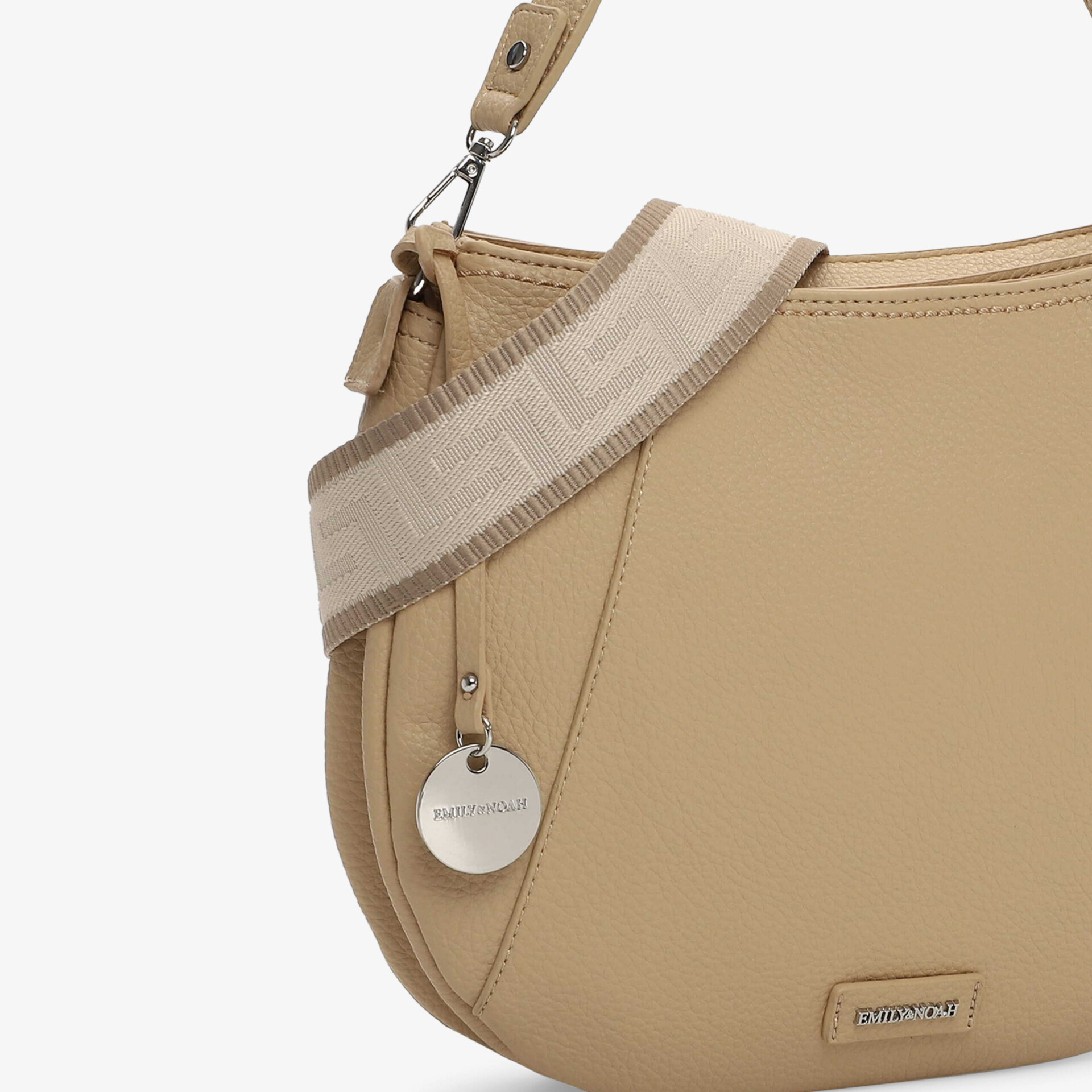 Detailansicht einer beigen Handtasche mit hochwertigem Logo-Accessoire und abnehmbarem Schulterriemen