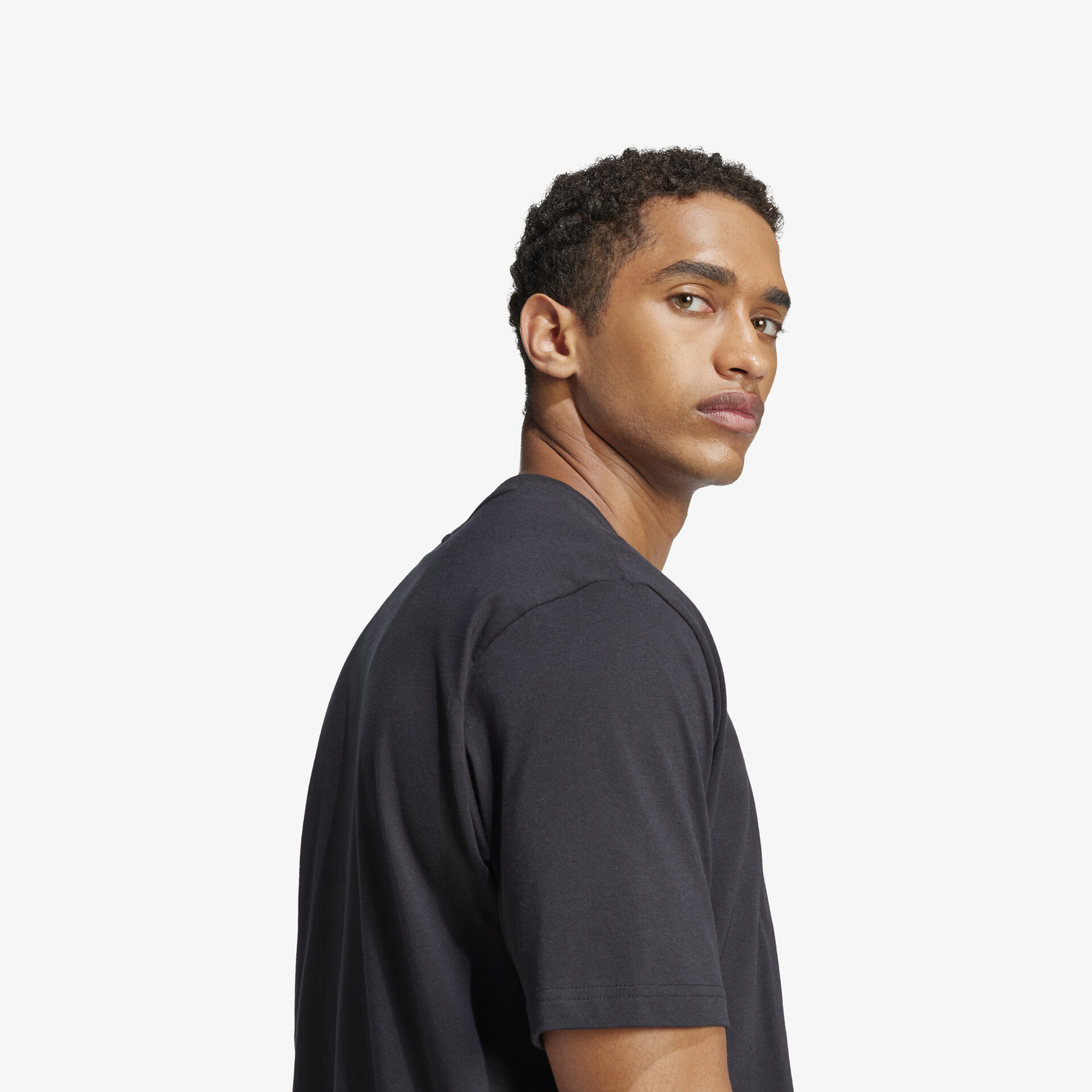 Seitliche Ansicht eines Mannes mit schwarzem T-Shirt, klarer Look, entspannter Stil, hochwertiges Material sichtbar