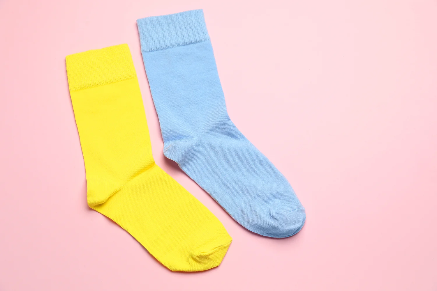 Zwei bunte Kindersocken, eine gelb und eine hellblau, flach liegend auf rosa Hintergrund