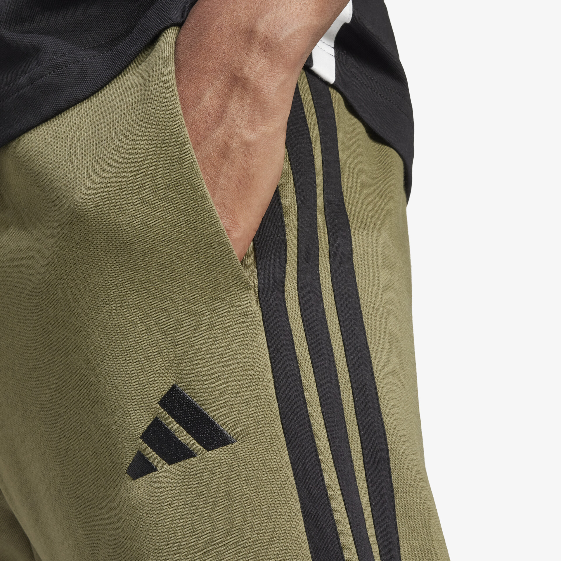 Detailaufnahme einer olivefarbenen Sporthose mit schwarzen Streifen und klar sichtbarem adidas Logo