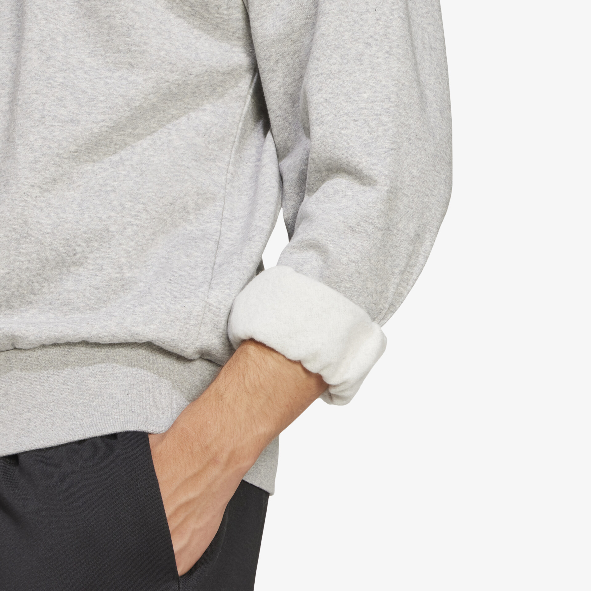 Detailaufnahme eines hellgrauen Sweatshirts mit aufgekrempeltem Ärmel und sichtbarer Hand in der Tasche