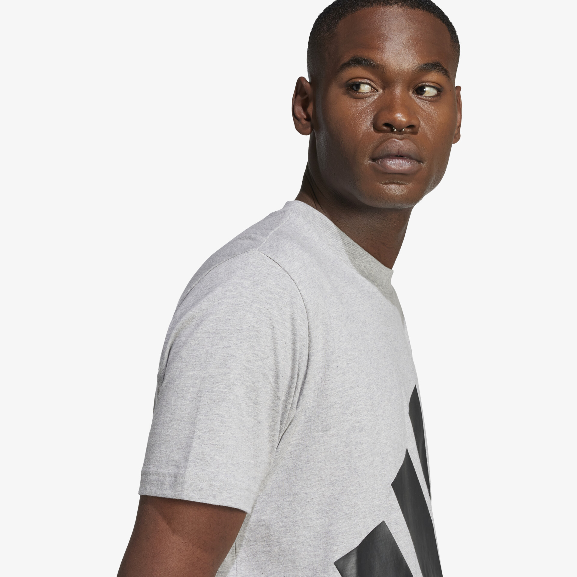 Seitliche Ansicht eines Modells trägt lässiges graues T-Shirt mit großem, auffälligem Logo auf der Brust