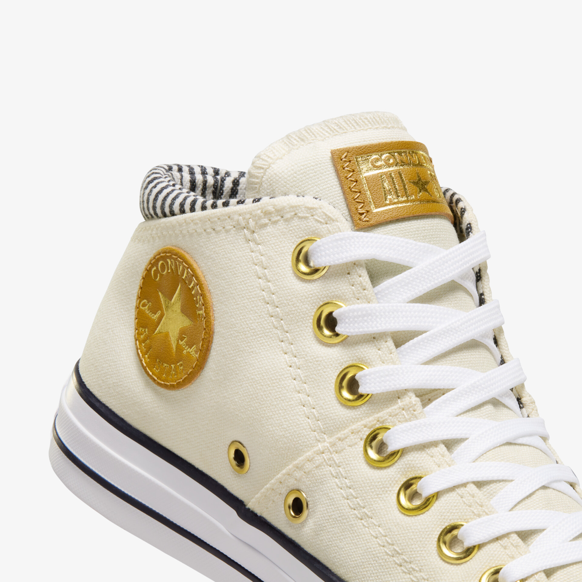 Detailaufnahme weißer Ledersneaker mit goldfarbenen Ösen und Logoplakette, klare Schnürung sichtbar
