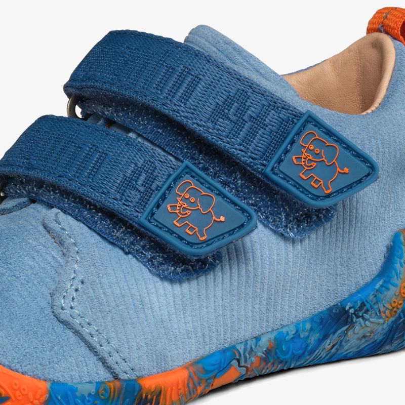 Detailaufnahme eines hellblauen Schuhs mit strukturiertem Material und zwei Klettverschlüssen, farbige Sohle sichtbar
