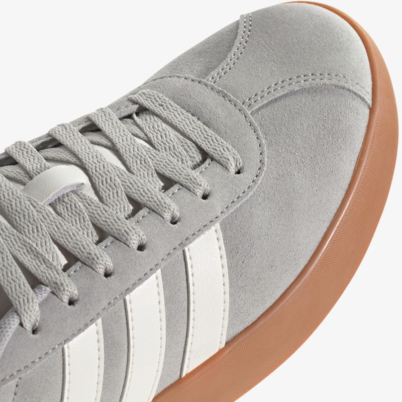 Detailaufnahme eines grauen Veloursleder-Sneakers mit weißen Streifen und brauner Gummisohle