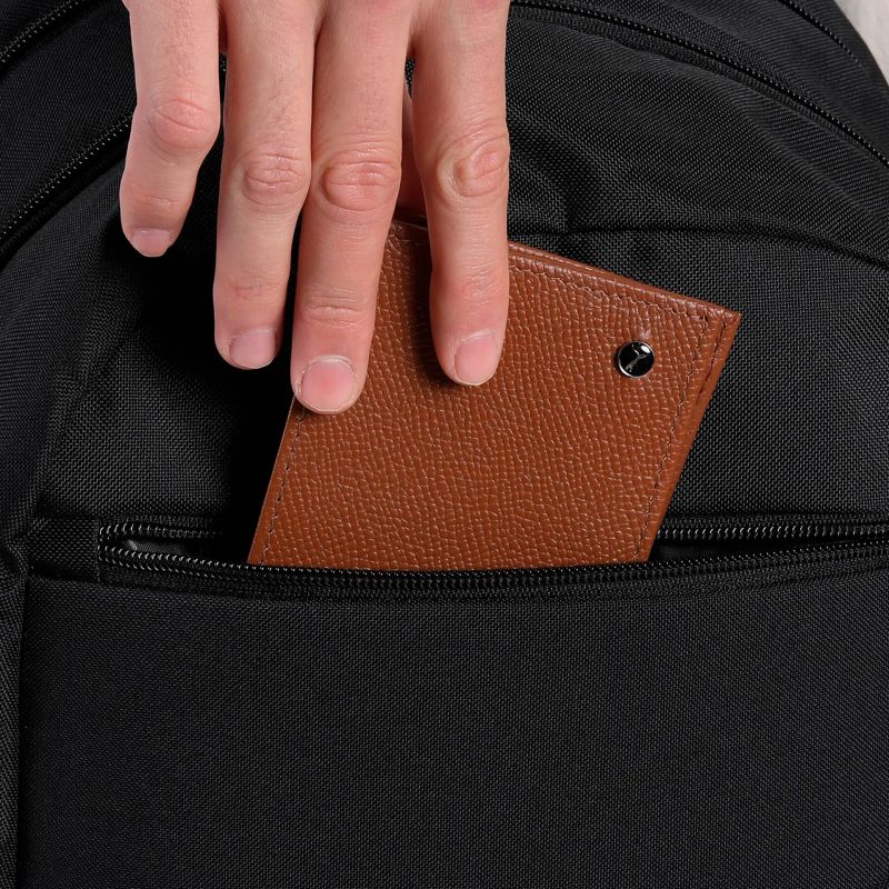 Kompakte braune Geldbörse aus hochwertigem Material wird in der vorderen Tasche eines schwarzen Rucksacks verstaut