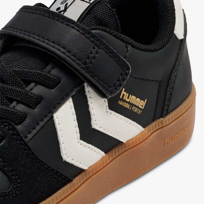 Schwarzer Sneaker mit weißem Chevron-Design, Klettverschluss und robuster brauner Gummisohle.