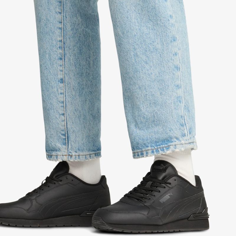 Schwarze sportliche Schuhe aus Leder mit Schnürsenkeln, getragen an den Füßen mit weißen Socken und Jeans