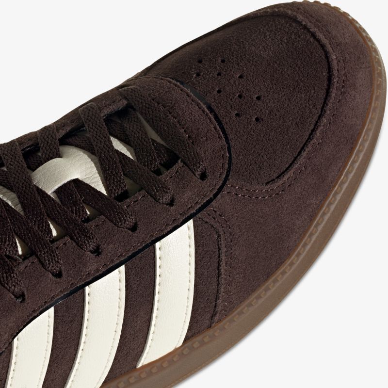 Detailaufnahme des vorderen Bereichs eines braunen Wildleder-Sneakers mit weißen Streifen und Schnürsenkeln